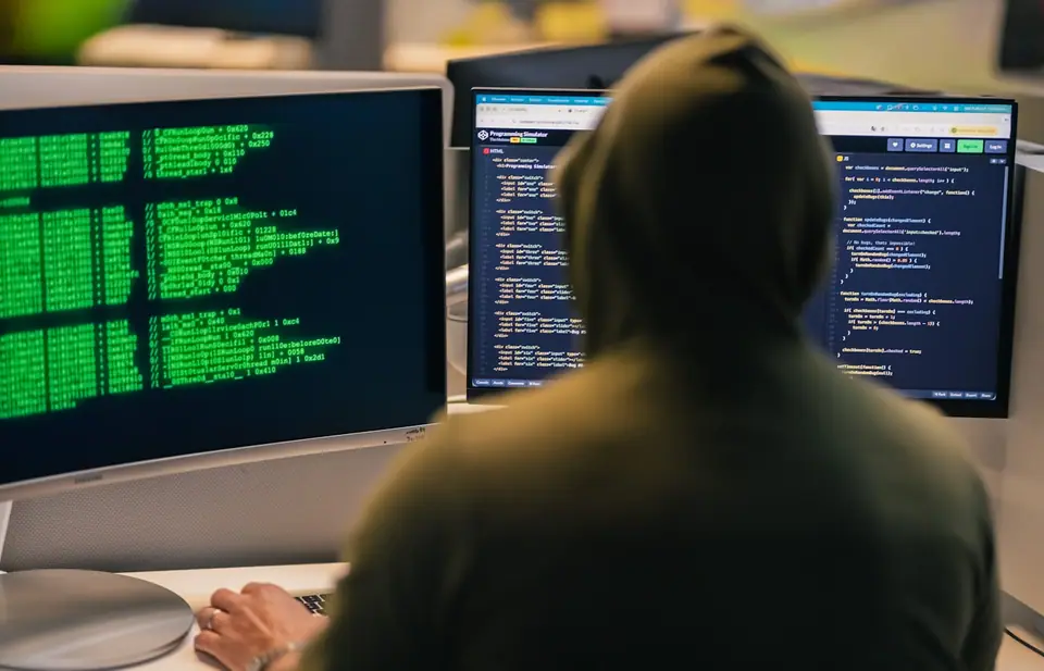 Persoon met capuchon achter een computerscherm vol code, van achteren gezien