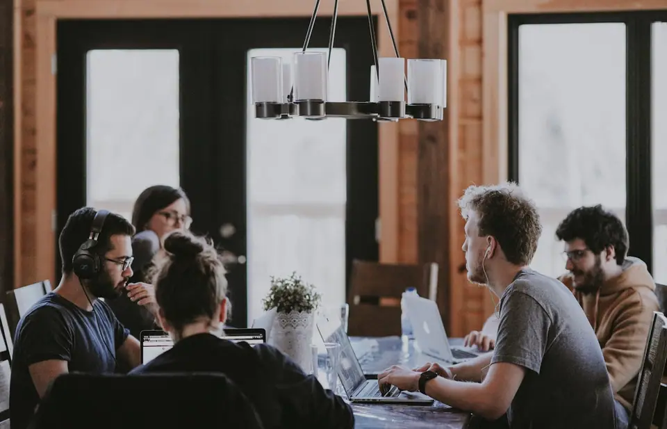 Twee mensen overleggen aan tafel met een laptop en papieren schetsen