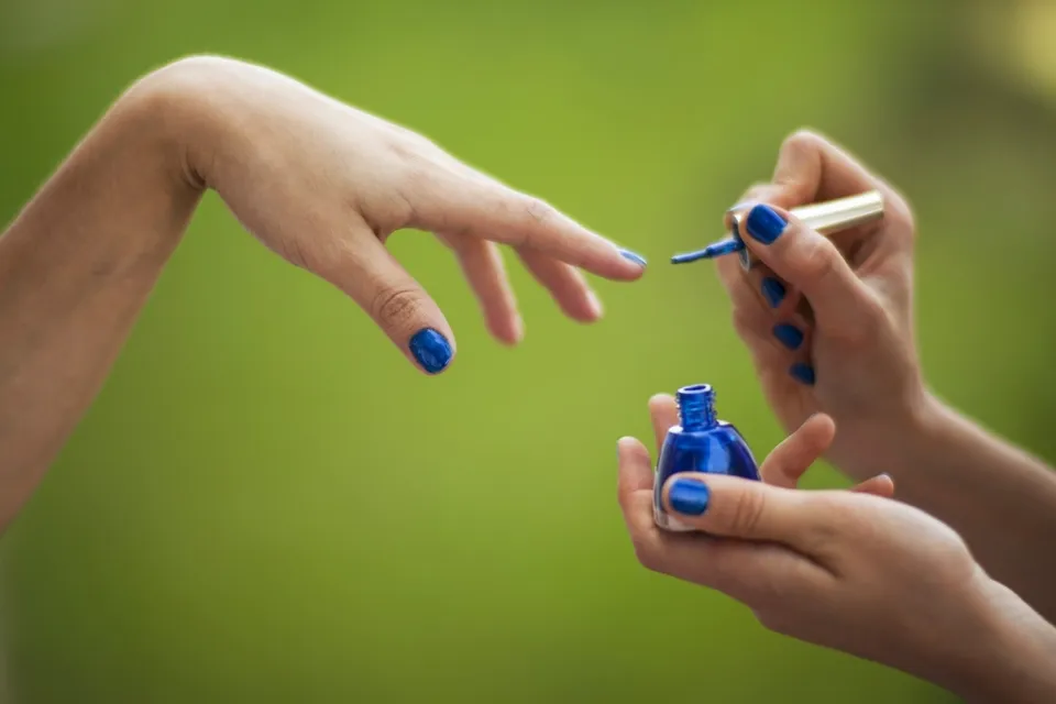Een manicure waarbij blauwe nagellak wordt aangebracht